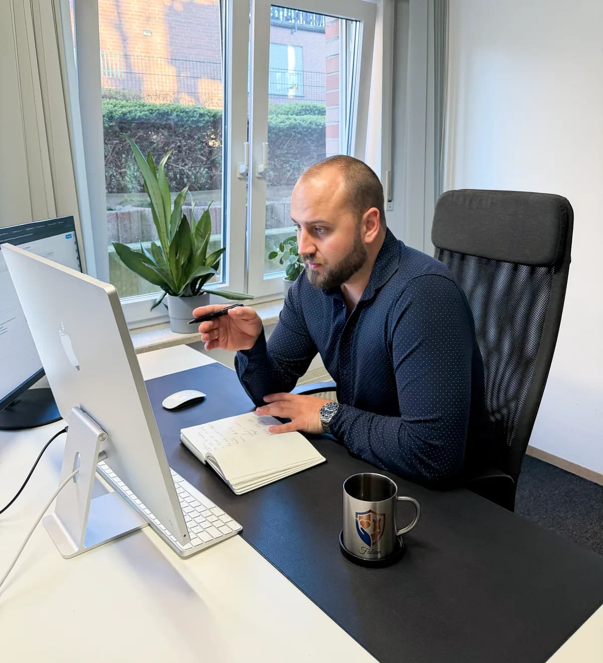 Fabian Bröggelhoff am Schreibtisch, den Stift in der Hand, im Gespräch vor dem Bildschirm